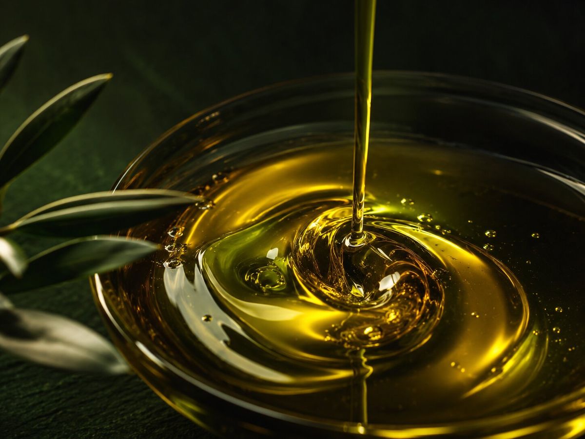 Olio extravergine d’oliva dorato che vortica in una ciotola di vetro scuro